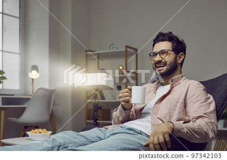 Cheerful man is watching comedy movie alone at home with help of movie projector. 97342103