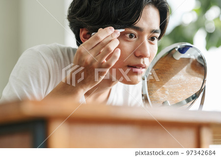 Young man trimming eyebrows with tweezers 97342684