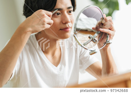 Young man trimming his eyebrows with scissors 97342688