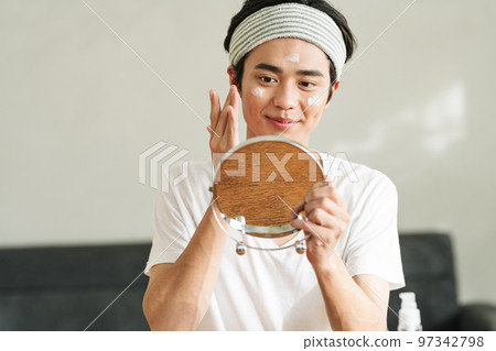 Young man applying moisturizing cream on his face 97342798