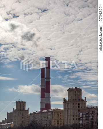 CHP in the city. Smoke rises into the sky from the heat pipes of the power plant. Pipe of combined heat and power plant CHP or cogeneration against background of multi-storey residential buildings 97342994