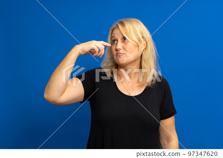 Photo of crazy amazed woman pointing index finger at herself, impressed, chooses news, isolated over blue tinted background. 97347620