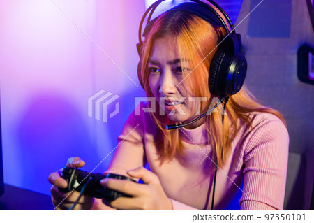 Gamer using joystick controller for virtual tournament plays online video game with computer neon lights, woman wear gaming headphones playing live stream esports games console at home, Esport concept 97350101