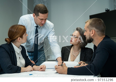 The boss gives instructions to three employees in the office conference room. Brainstorming engineers and architects. The boss gives instructions to three employees in the office conference room. Brainstorming engineers and architects. 97351296