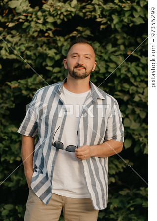 A man is posing in the garden. A guy with green leaves in the background. 97355299