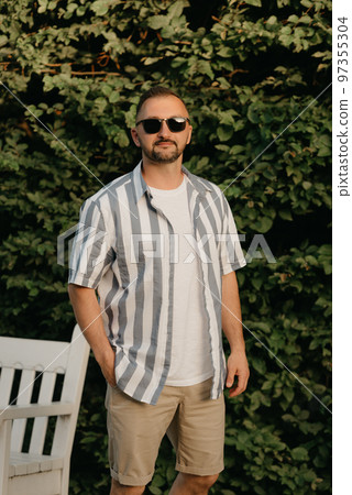 A man is posing in the garden. A guy with green leaves in the background. 97355304