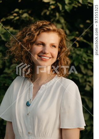 A woman with curly hair is posing in the park at the sunset. A woman with curly hair is posing in the park at the sunset. 97355325