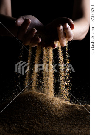 Hand releasing dropping sand. Fine Sand flowing pouring through fingers against black background. Summer beach holiday vacation and time passing concept. Isolated high speed shutter Hand releasing dropping sand. Fine Sand flowing pouring through fingers against black background. Summer beach holiday vacation and time passing concept. Isolated high speed shutter 97356261