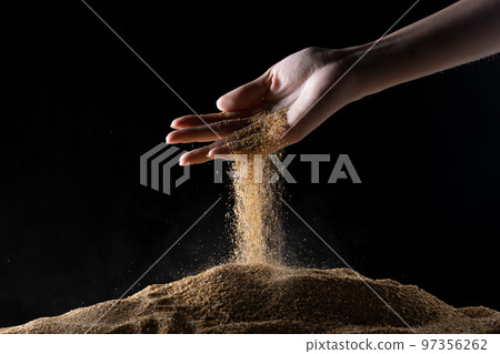 Hand releasing dropping sand. Fine Sand flowing pouring through fingers against black background. Summer beach holiday vacation and time passing concept. Isolated high speed shutter 97356262