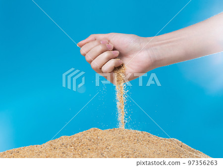 Hand releasing dropping sand. Fine Sand flowing pouring through fingers against blue background. Summer beach holiday vacation and time passing concept. Isolated high speed shutter Hand releasing dropping sand. Fine Sand flowing pouring through fingers against blue background. Summer beach holiday vacation and time passing concept. Isolated high speed shutter 97356263