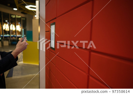 A woman scans a red code to pick up a parcel at a parcel machine. Automated Postal Box. 97358614
