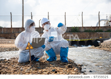 Ecologist sampling taken dead fish to inspaction and save data to laptop computer, Biologist wear protective suit and mask collects sample of waste water from industry, problem environment 97359325