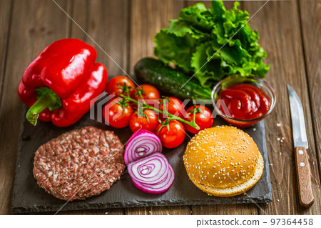 High angle view of ingredients for classic beef burger on stone board with knife. Selective focus. High angle view of ingredients for classic beef burger on stone board with knife. Selective focus. 97364458