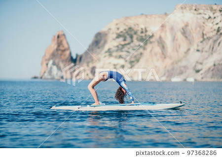 Woman sup yoga. Middle age sporty woman practising yoga pilates on paddle sup surfboard. Female stretching doing workout on sea water. Modern individual female hipster outdoor summer sport activity. Woman sup yoga. Middle age sporty woman practising yoga pilates on paddle sup surfboard. Female stretching doing workout on sea water. Modern individual female hipster outdoor summer sport activity. 97368286