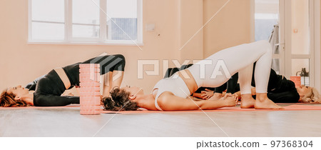 Middle aged well looking women, performing fascia exercises on the floor using a massage foam roller - tool to relieve tension in the back and relieve muscle pain. Female fitness yoga routine concept Middle aged well looking women, performing fascia exercises on the floor using a massage foam roller - tool to relieve tension in the back and relieve muscle pain. Female fitness yoga routine concept 97368304