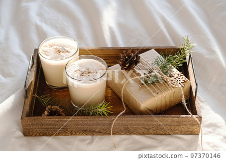 Christmas cozy morning in bed. Gift box and eggnog on wooden tray on white bedding. Christmas cozy morning in bed. Gift box and eggnog on wooden tray on white bedding. 97370146