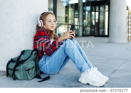 Young smiling beautiful hipster happy teen girl in city street,speaking on smartphone,headphones, jeans, backpack, positive, spring trend, urban teenage style Young smiling beautiful hipster happy teen girl in city street,speaking on smartphone,headphones, jeans, backpack, positive, spring trend, urban teenage style 97378177