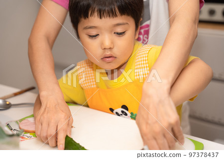 A 4-year-old boy being taught by his mother how to cut a cucumber A 4-year-old boy being taught by his mother how to cut a cucumber 97378437