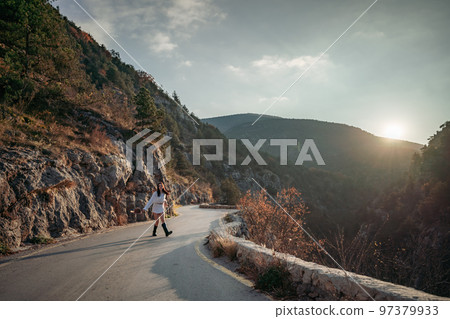 The woman is dear to the mountains. A woman in a white sweater, black boots and a hat walks along a winding alpine path between the mountains at the end of summer at sunset. Travel concept. The woman is dear to the mountains. A woman in a white sweater, black boots and a hat walks along a winding alpine path between the mountains at the end of summer at sunset. Travel concept. 97379933