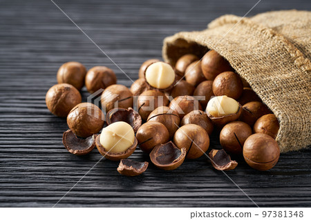 Macadamia are poured out of the bag on a black table, close-up. Macadamia are poured out of the bag on a black table, close-up. 97381348