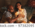 Happy interracial couple celebrating New Year at home together, sitting by Christmas tree 97382095