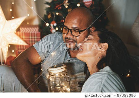 Happy interracial couple celebrating New Year at home together, sitting by Christmas tree Happy interracial couple celebrating New Year at home together, sitting by Christmas tree 97382096