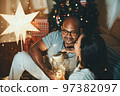Happy interracial couple celebrating New Year at home together, sitting by Christmas tree 97382097