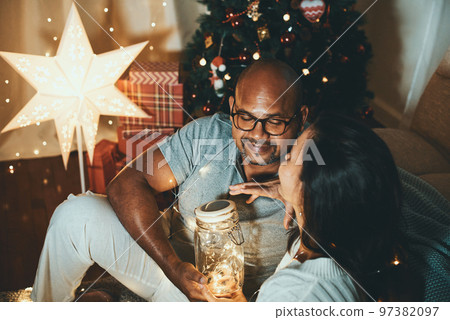 Happy interracial couple celebrating New Year at home together, sitting by Christmas tree Happy interracial couple celebrating New Year at home together, sitting by Christmas tree 97382097