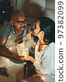Happy interracial couple celebrating New Year at home together, sitting by Christmas tree 97382099