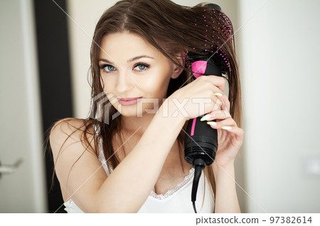 Woman drying hair with hair dryer and round brush. 97382614