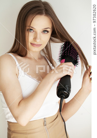 Woman drying long brown hair with blow dryer and round brush Woman drying long brown hair with blow dryer and round brush 97382620