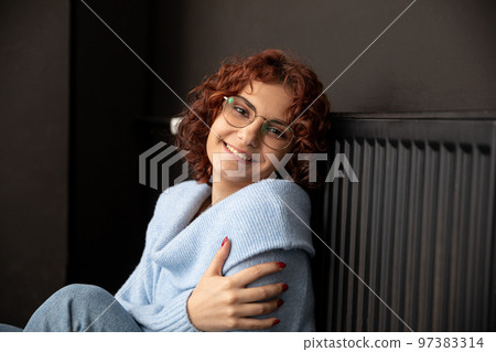 A smiling girl sits and leans against a hot radiator. 97383314