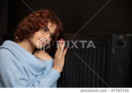 A frozen girl hugs a hot radiator to warm herself. 97383316