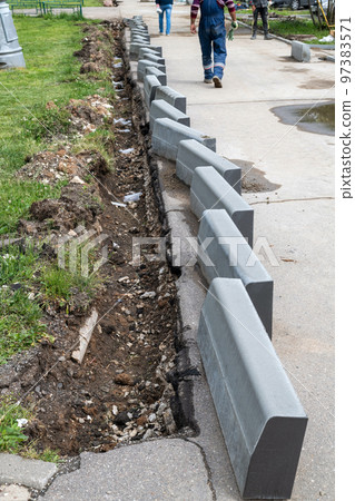 New curbs stand at the edge of the sidewalk. Preparing to repair road New curbs stand at the edge of the sidewalk. Preparing to repair road 97383571