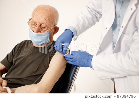 Senior gentleman on a wheelchair isolated on a white background. Man wearing khaki t-shirt and doctor wearing white medical gown and face mask. Doctor stick a band-aid after a vaccination against 97384790