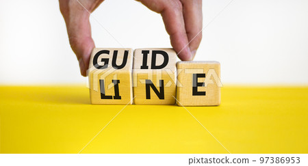 Guideline symbol. Concept word Guideline on wooden blocks. Businessman hand changes words Guide on Line. Beautiful yellow table white background. Business and guideline concept. Copy space. 97386953