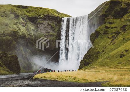 Famous Skogafoss waterfall on Skoga river - tourists standing in front and watching waterfall 97387688