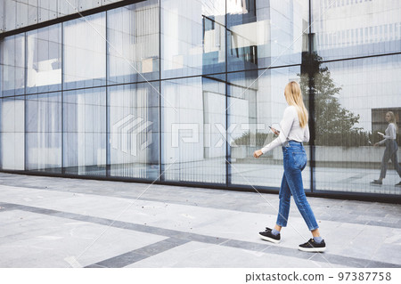 Woman walking by the side of a glass office building while on a break Woman walking by the side of a glass office building while on a break 97387758