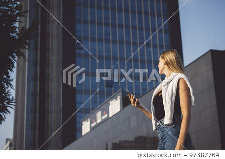 Young blonde woman in an urban setting using a mobile device 97387764