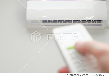 Man's hand using remote controler. Hand holding remote and adjusting temperature of air conditioner mounted on a white wall. Man's hand using remote controler. Hand holding remote and adjusting temperature of air conditioner mounted on a white wall. 97388770