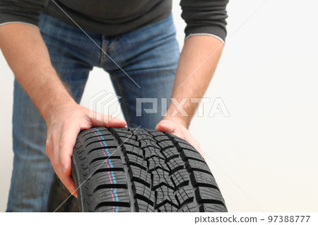 Closeup of mechanic hands pushing a black tire on a white background. Replacement of winter and summer tires. Cropped Hands Of Mechanic. Closeup of mechanic hands pushing a black tire on a white background. Replacement of winter and summer tires. Cropped Hands Of Mechanic. 97388777