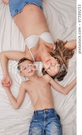a little son and his pregnant mother are lying in bed together. Family fun. Soft focus a little son and his pregnant mother are lying in bed together. Family fun. Soft focus 97389253