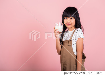 Asian little kid 10 years old smile hold milk glass drink white milk at studio shot isolated on pink background, Happy child girl daily life health care Medicine food 97390875
