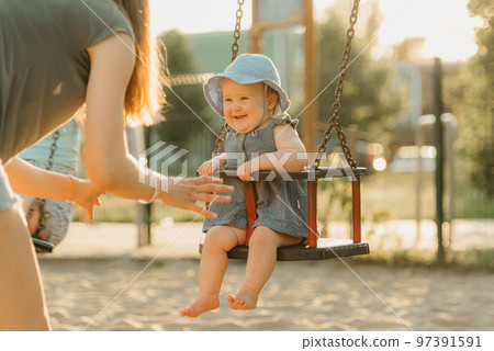 Toddler baby girl is joying on a swing on the warm summer evening Toddler baby girl is joying on a swing on the warm summer evening 97391591