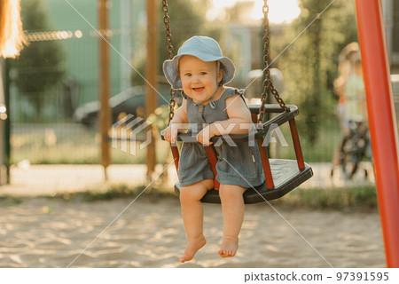 Toddler baby girl in a dress on a swing on the warm summer evening 97391595