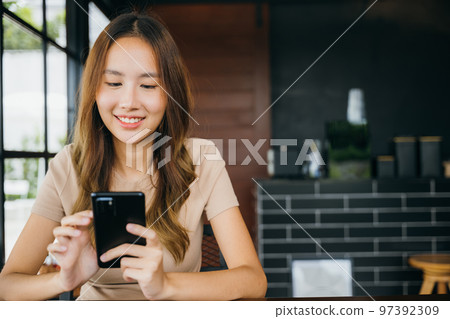 Beautiful Asian female hands holding and typing to communicate with others through on mobile phone, young woman using smartphone for shopping online at cafe coffee shop near windows in morning 97392309