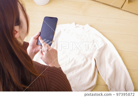 一個年輕女人在她的智能手機上賣跳蚤市場 一個年輕女人在她的智能手機上賣跳蚤市場 97395872