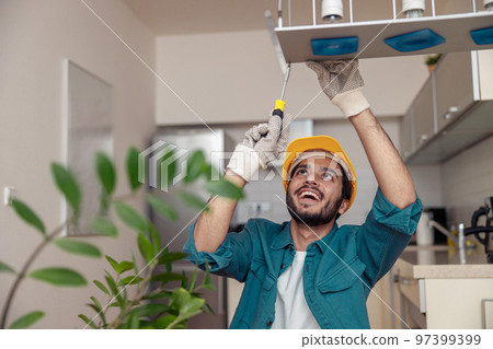 Professional electrician worker in uniform is installing electric lamps light in kitchen Professional electrician worker in uniform is installing electric lamps light in kitchen 97399399