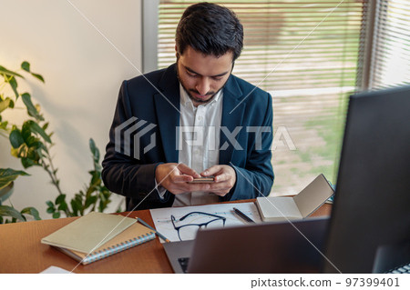 Focused indian businessman in suit use phone while working from home office  97399401