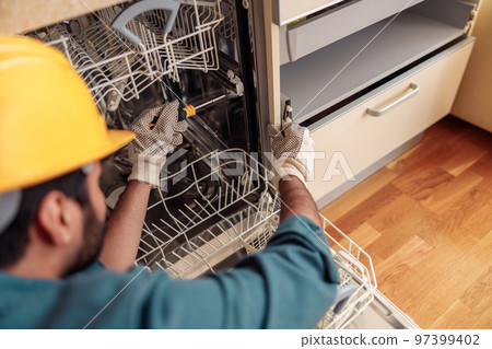 Close up of handyman in special clothing repairing dishwasher in modern kitchen Close up of handyman in special clothing repairing dishwasher in modern kitchen 97399402